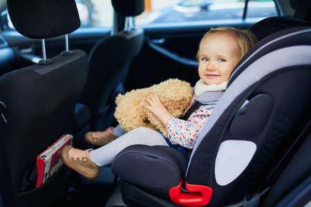 Adorable toddler girl in modern car seat with her favorite stuffed toy. Little kid traveling by car. Child safety on the road. Trip with a babyの写真素材