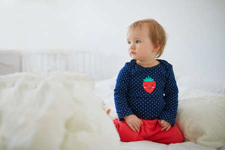 Adorable toddler girl sitting on bed. Happy healthy little child at home. Infant kid in sunny...
