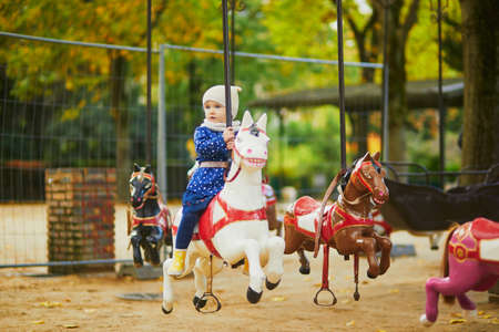 Toddler having fun on vintage French merry-go-round in Paris. Adorable little girl on the playground. Outdoor activities for small kidsの写真素材