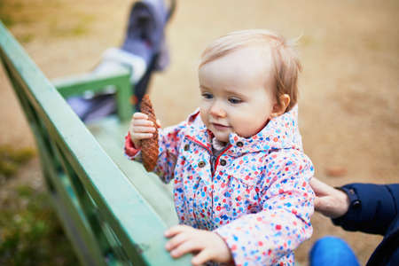One year old girl playing with spruce cone in park. Toddler having fun on a spring day outdoors....