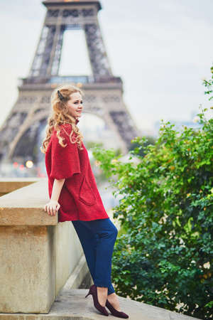 Young woman with long blond curly hair in Paris, France. Beautiful tourist in red coat near the Eiffel towerの写真素材