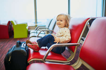 Adorable little toddler girl traveling by plane. Child sitting in gate and waiting for the flight. Traveling abroad with kids. Unaccompanied minor conceptの写真素材
