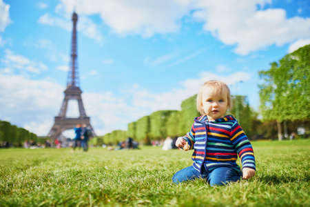 One year old girl sitting on the grass in Paris, with the Eiffel tower behind her. Little kid enjoying summer day in Franceの写真素材