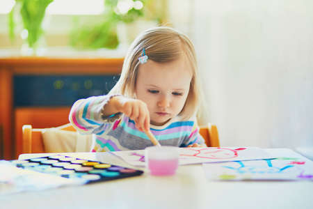 Adorable little girl painting with aquarelle at home, in kindergaten or preschool. Creative games...