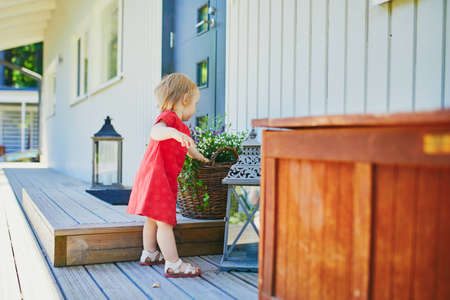 Adorable baby girl in red dress having fun outdoors on her house terrace on a sunny summer dayの写真素材