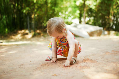 Adorable little girl outdoors in park on a sunny day. Toddler looking playing with sand. Kid exploring natureの写真素材