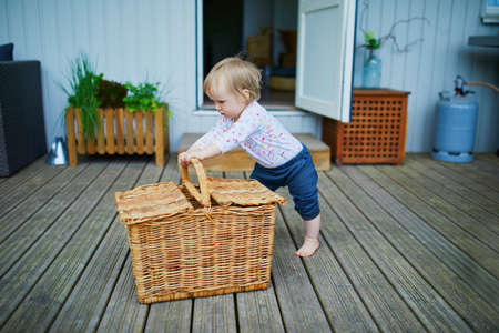 Adorable baby girl having fun with basket outdoors on her house terrace on a sunny summer day