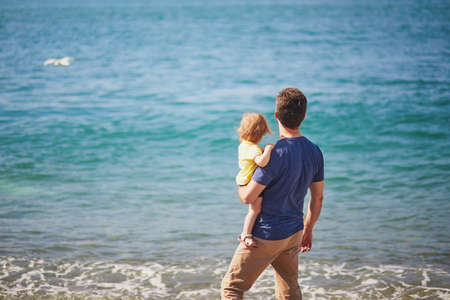 Man with adorable toddler girl looking at the ocean in Etretat, Normandy, France. Father and daughter travelling together. Family of two having fun on the beachの写真素材