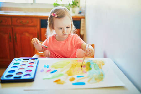 Adorable little girl drawing with colorful aquarelle paints at home, in kindergaten or preschool. Creative games, education and distance learning for kids. Stay at home entertainmentの写真素材