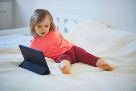 Toddler girl with digital tablet at home. Child watching cartoons. Kid using gadget to communicate...
