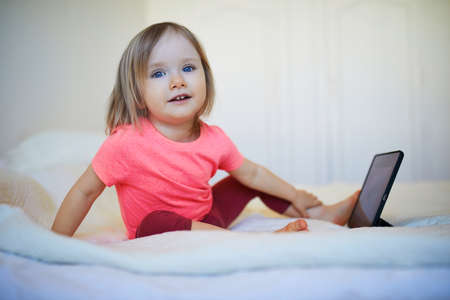 Toddler girl with digital tablet at home. Child watching cartoons. Kid using gadget to communicate...