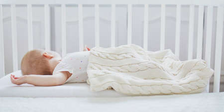 Adorable baby girl sleeping in co-sleeper crib attached to parents' bed. Little child having a day...