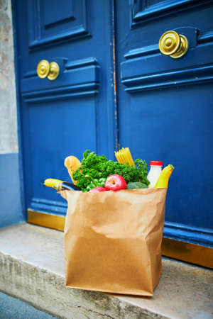 Food delivery during coronavirus outbreak. Paper bag with grocery order in front of the door in Paris, France during Covid-19 epidemic. Safe online shopping, food donation or takeout meal conceptの写真素材