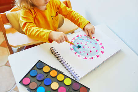 Adorable little girl drawing coronavirus with colorful aquarelle paints at home. Creative games, education and distance learning for kids. Stay at home entertainmentの写真素材