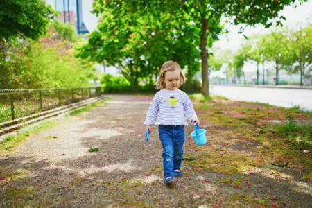 Adorable toddler girl playing with bucket and shovel, making mudpies and gathering small stones. Outdoor creative activities for kidsの写真素材