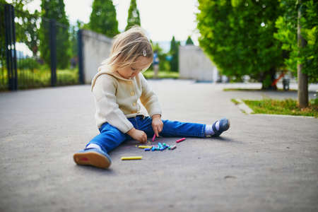 Adorable toddler girl drawing with colorful chalks on asphalt. Outdoor activity and creative games for small kidsの写真素材
