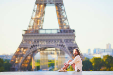 Beautiful young girl sitting near the Eiffel tower in Paris. Tourist enjoying her vacation in France