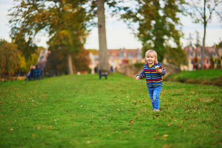 Adorable cheerful toddler girl running in autumn park in Paris, France. Happy child enjoying warm and sunny fall day. Outdoor autumn activities for kidsの写真素材