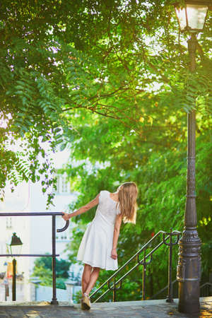 Beautiful young woman in white dress walking on famous Montmartre hill in Paris, France at early morningの写真素材