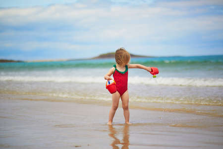 Adorable toddler girl playing on the sand beach at Atlantic coast of Brittany, France. Small child enjoying vacation by the sea or ocean. Travelling with kidsの写真素材