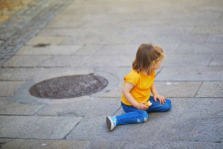 Unhappy and emotional toddler girl sitting on the floor outdoors. Misbehaving child on the street. Terrible twos and kid tantrums conceptの写真素材