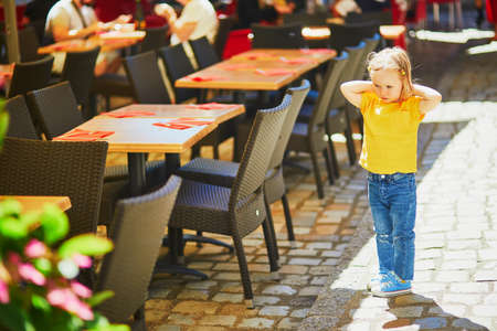 Unhappy and stubborn toddler girl in outdoor restaurant. Misbehaving child outdoors. Terrible twos and kid tantrums conceptの写真素材