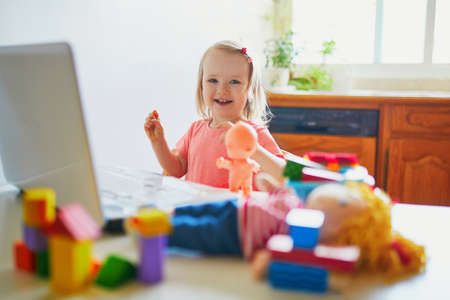 Happy toddler girl with laptop and toys. Kid using computer to communicate with friends, elderly relatives or kindergartners. Education or online communication for kids. Stay at home entertainmentの写真素材