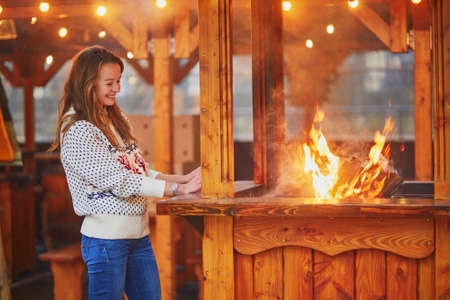 Beautiful young woman warming hands near fire on traditional Christmas market in Paris, Franceの写真素材