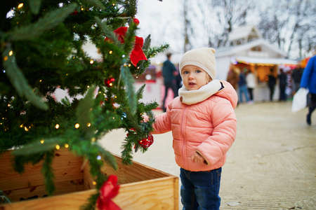 Adorable toddler girl on Christmas market in Paris. Happy child having fun outdoors during seasonal holidays. Celebrating xmas and New Year with kidsの写真素材