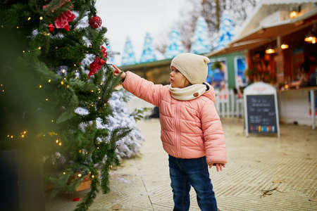 Adorable toddler girl on Christmas market in Paris. Happy child having fun outdoors during seasonal holidays. Celebrating xmas and New Year with kidsの写真素材