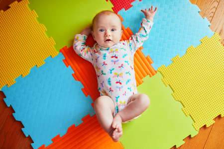 4 months old baby girl lying on colorful play mat on the floor. Activity carpet for kidsの写真素材
