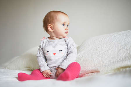Baby girl sitting on bed. Happy healthy little child at home. Infant kid in sunny nurseryの写真素材