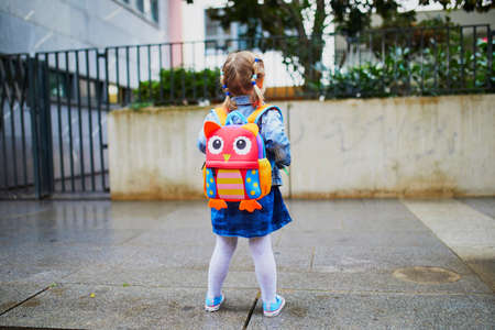Adorable toddler girl with funny backpack ready to go to daycare, kindergarten or school. First day of school conceptの写真素材