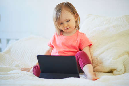 Toddler girl with digital tablet at home. Child watching cartoons. Kid using gadget to communicate...
