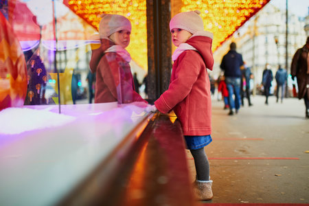 Toddler girl looking at window glass of large department store decorated for Christmas. Child enjoying holiday season in Paris, Franceの写真素材