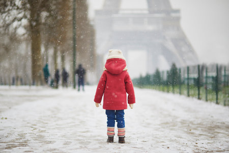 Adorable toddler girl near the Eiffel tower on a day with heavy snowfall in Paris, France. Happy child playing with snow. Winter activities for kids.の写真素材