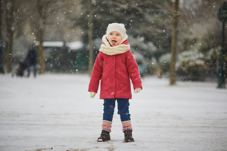 Adorable toddler girl on a day with heavy snowfall. Happy child playing with snow. Winter activities for kids.の写真素材