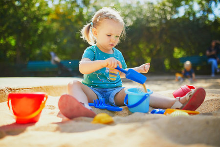 Adorable little girl having fun on playground in sandpit. Toddler playing with sand molds and making mudpies. Outdoor creative activities for kidsの写真素材