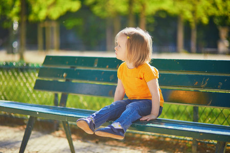Two year old girl sitting on the bench in Paris, France. Child walking in a city on a warm summer day. Outdoor activities for kidsの写真素材