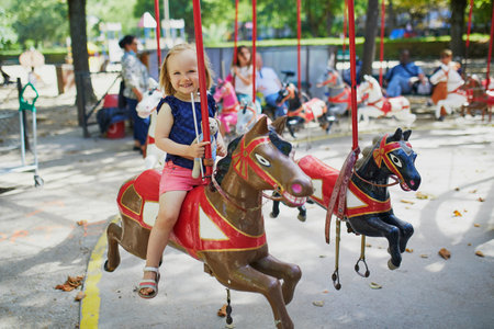 Adorable little girl on the playground. Toddler having fun on vintage French merry-go-round in Paris. Outdoor activities for small kidsの写真素材