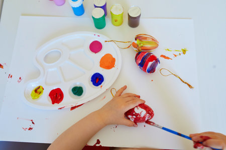 Adorable little girl painting eggs for Easter at home, in kindergaten or preschool. Celebrating holidays with children. Creative activities and games for kids. Stay at home entertainmentの写真素材