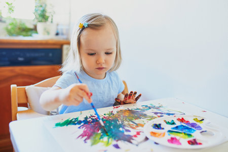 Adorable little girl drawing with colorful aquarelle paints at home, in kindergaten or preschool. Creative activities and games for kids. Stay at home entertainmentの写真素材