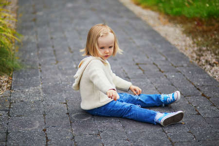 Unhappy and emotional toddler girl sitting on the floor outdoors. Misbehaving child on the street. Terrible twos and kid tantrums conceptの写真素材