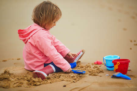 Adorable toddler girl playing on the sand beach at Atlantic coast of Brittany, France. Small child enjoying vacation by the sea or ocean. Travelling with kidsの写真素材
