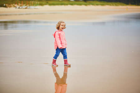 Adorable toddler girl on the sand beach at Atlantic coast of Brittany, France. Small child enjoying vacation by the sea or ocean. Travelling with kidsの写真素材