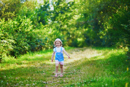 Adorable toddler girl having fun outdoors on a sunny summer day. Happy child walking in forest....
