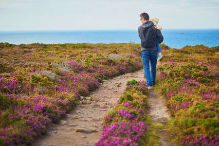 Man and toddler girl walking in heather meadows on Cape d'Erquy, one of the most popular tourist destinations in Brittany, France. Father and daughter travelling together. Family activitiesの写真素材