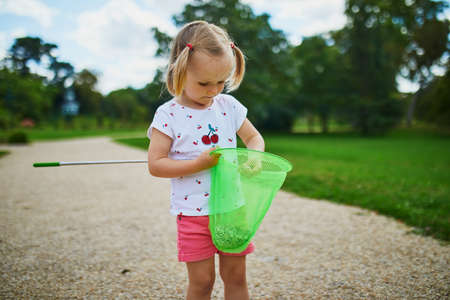 Adorable toddler girl playing with butterfy net outdoors on a summer day. Child gathering pebbles in scoop-net. Outdoor summer activities for kids.の写真素材