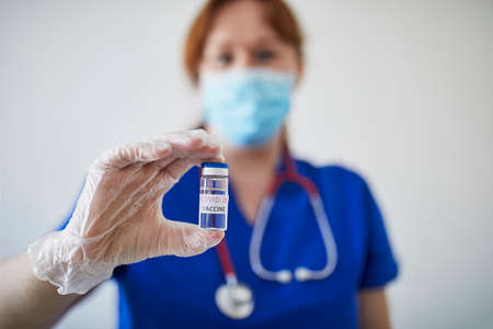 Female doctor or nurse with stethoscope, wearing face mask and sterile gloves, holding vial with COVID-19 vaccine. Research, clinical trial, vaccination or herd immunity conceptの写真素材