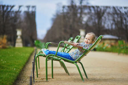 Happy cheerful toddler girl sitting on green chair in Tuileries Garden of Paris, Franceの写真素材